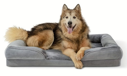 A larger, brown and black dog sitting upright in grey dog bed