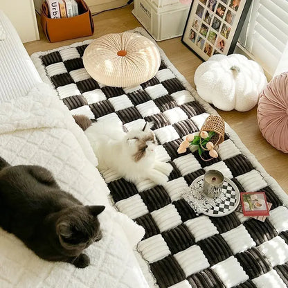 "Two cats lounging on a black checkered pet couch cover."
