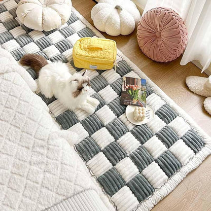 "Cat on a light grey quilted pet couch cover on the floor."
