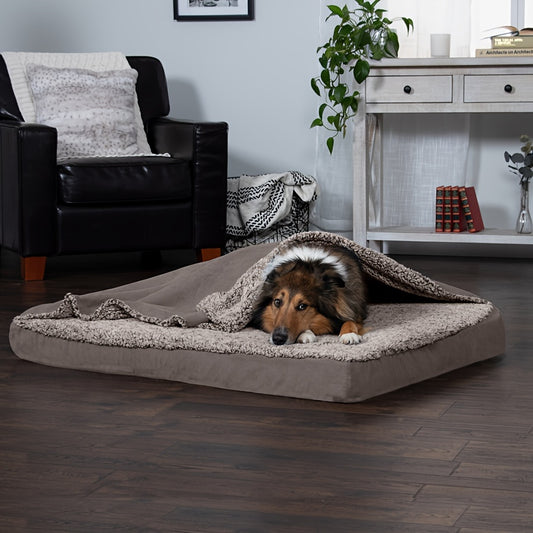 A fluffy dog is half-hidden under a blanket in a large, plush dog bed