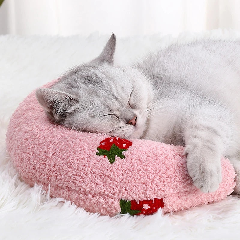 "Adorable cat snuggled comfortably in a pink U-shaped pillow, looking content."
