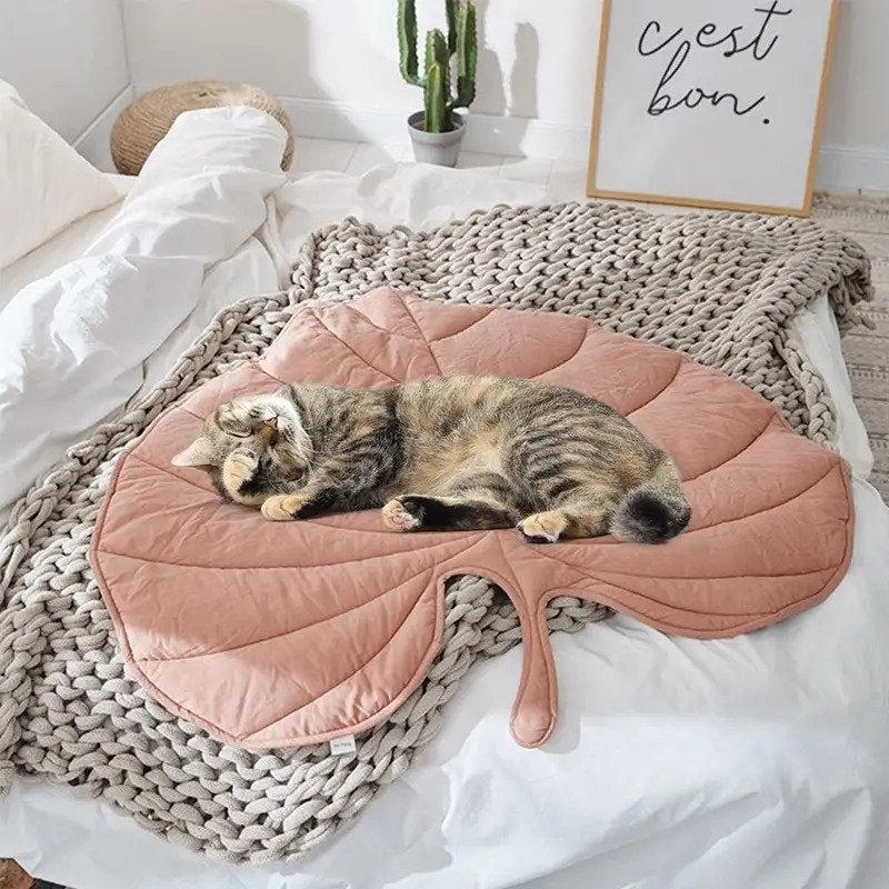 "Cat lounging on a soft pink quilted leaf-designed pet mat."